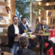 en panelsamtale med tre menn som sitter ved høye bord i et bibliotek