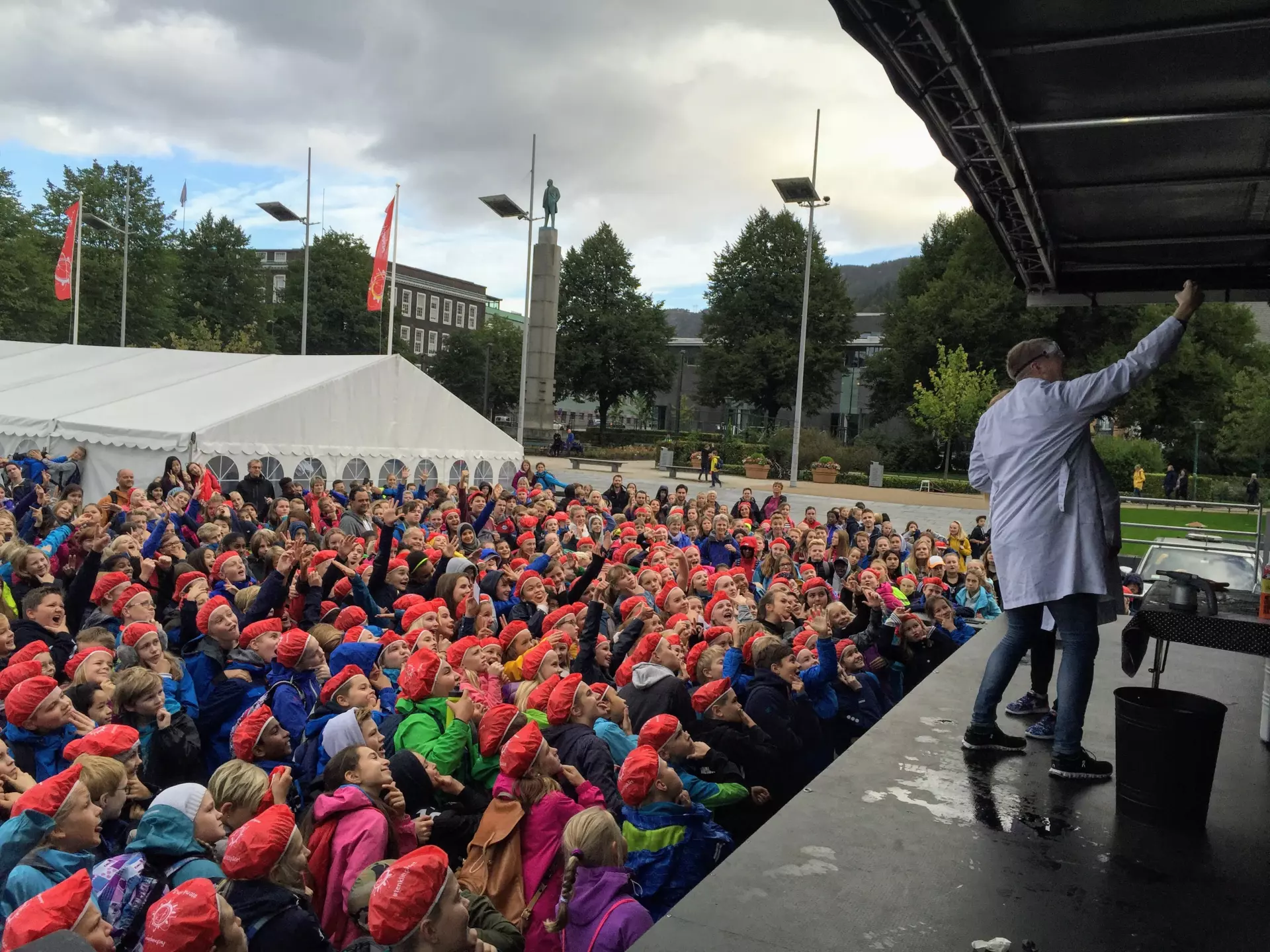 Forsker på scenen tar en selfie med mange skolebarn som har på seg røde sykkeltrekk på hodet.