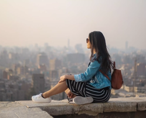Jente som sitter med solbriller på og stirrer utover en storby i tåke