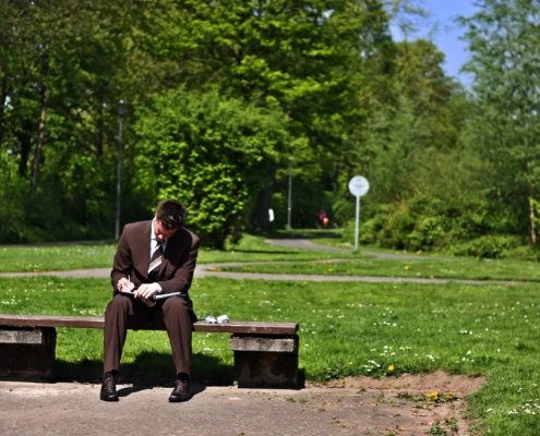 Man sitter på benk i park i dress og skriver på en skriveblokk.