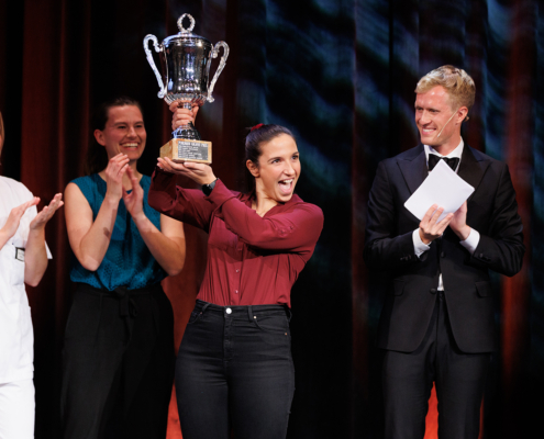 Vinner av Forsker Grand Prix Josepine Salice holder opp pokalen hun vant, mens de andre deltakerne og programleder applauderer.